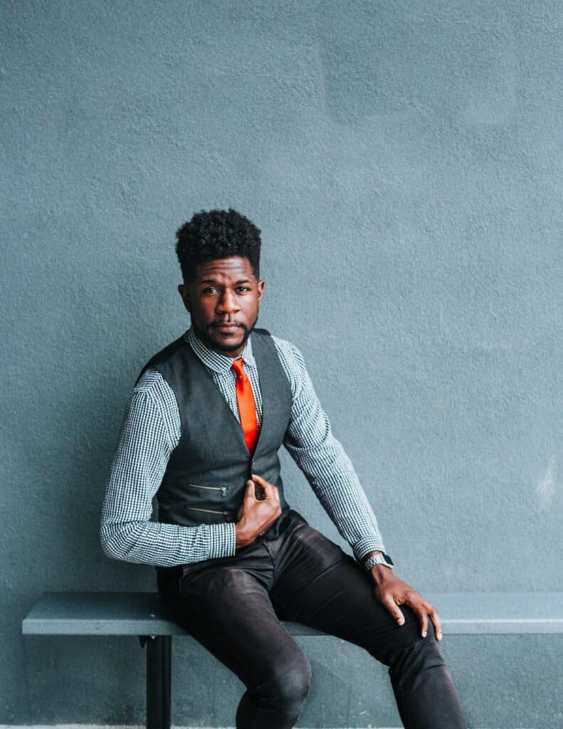 black man wearing vest and bright tie sitting on bench