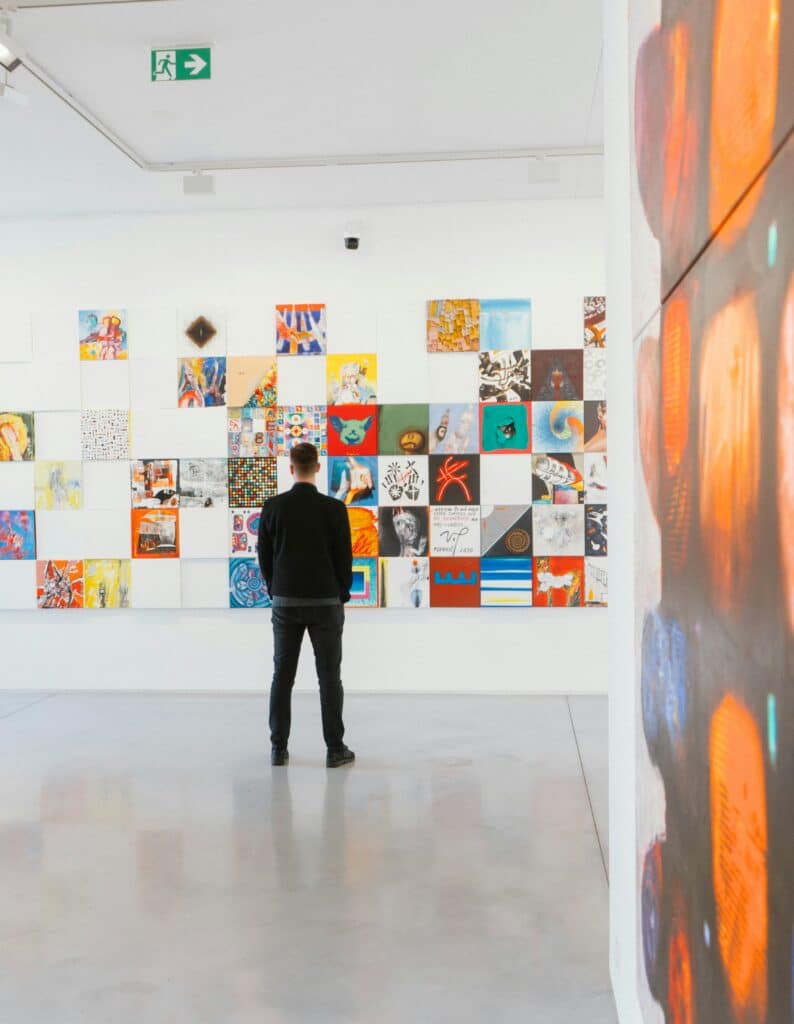 man in black jacket and pants looking at colorful modern and abstract art displayed on the white walls of a gallery