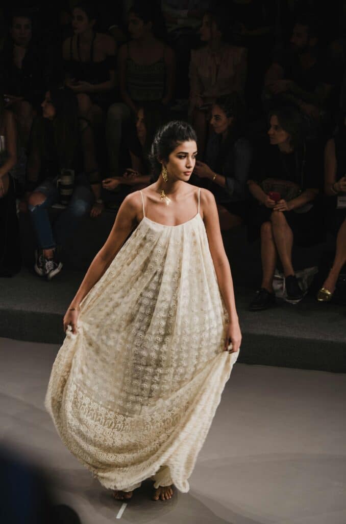 model turning on runway holding the skirt of her flowy textured cream dress