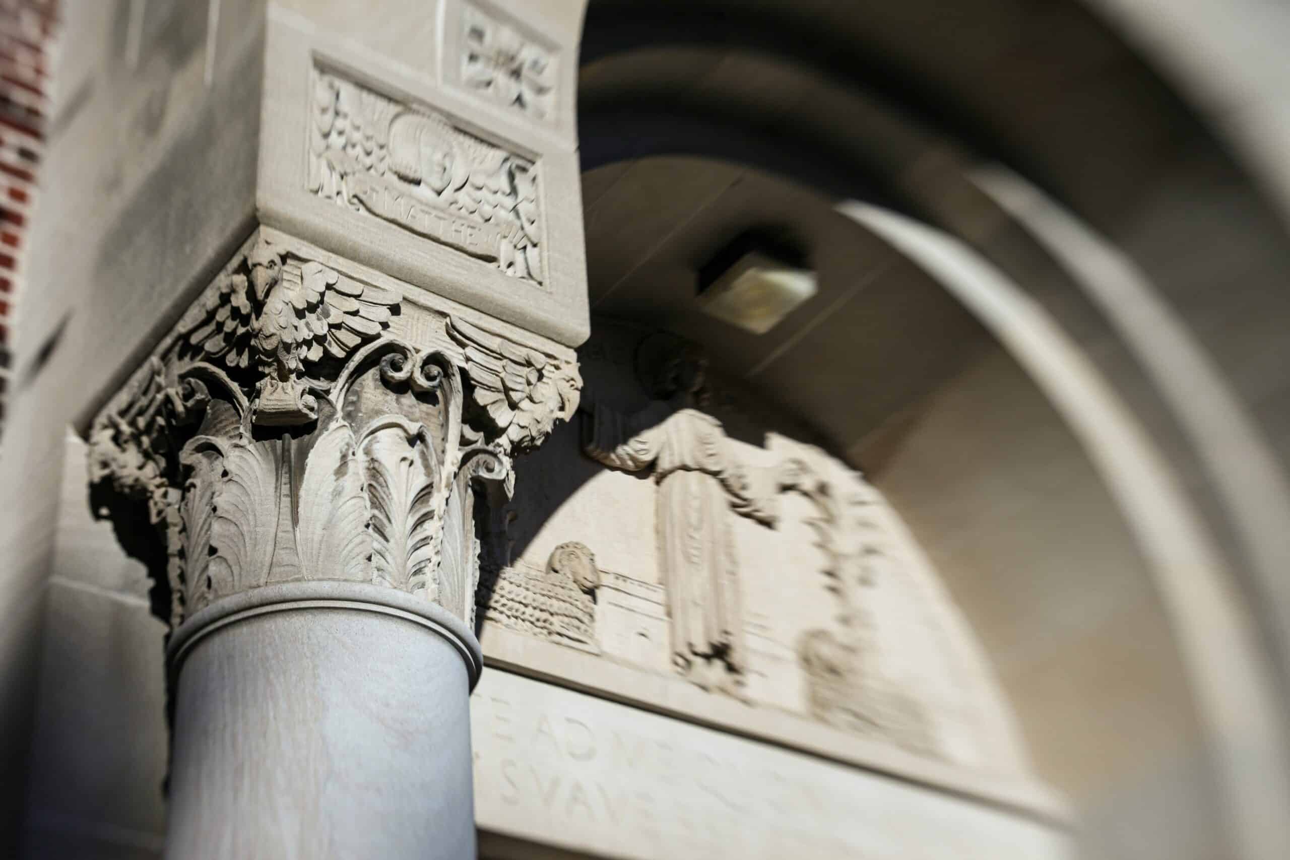 Foto de mudança de inclinação com foco nos detalhes arquitetônicos de um pilar de pedra em um campus universitário.