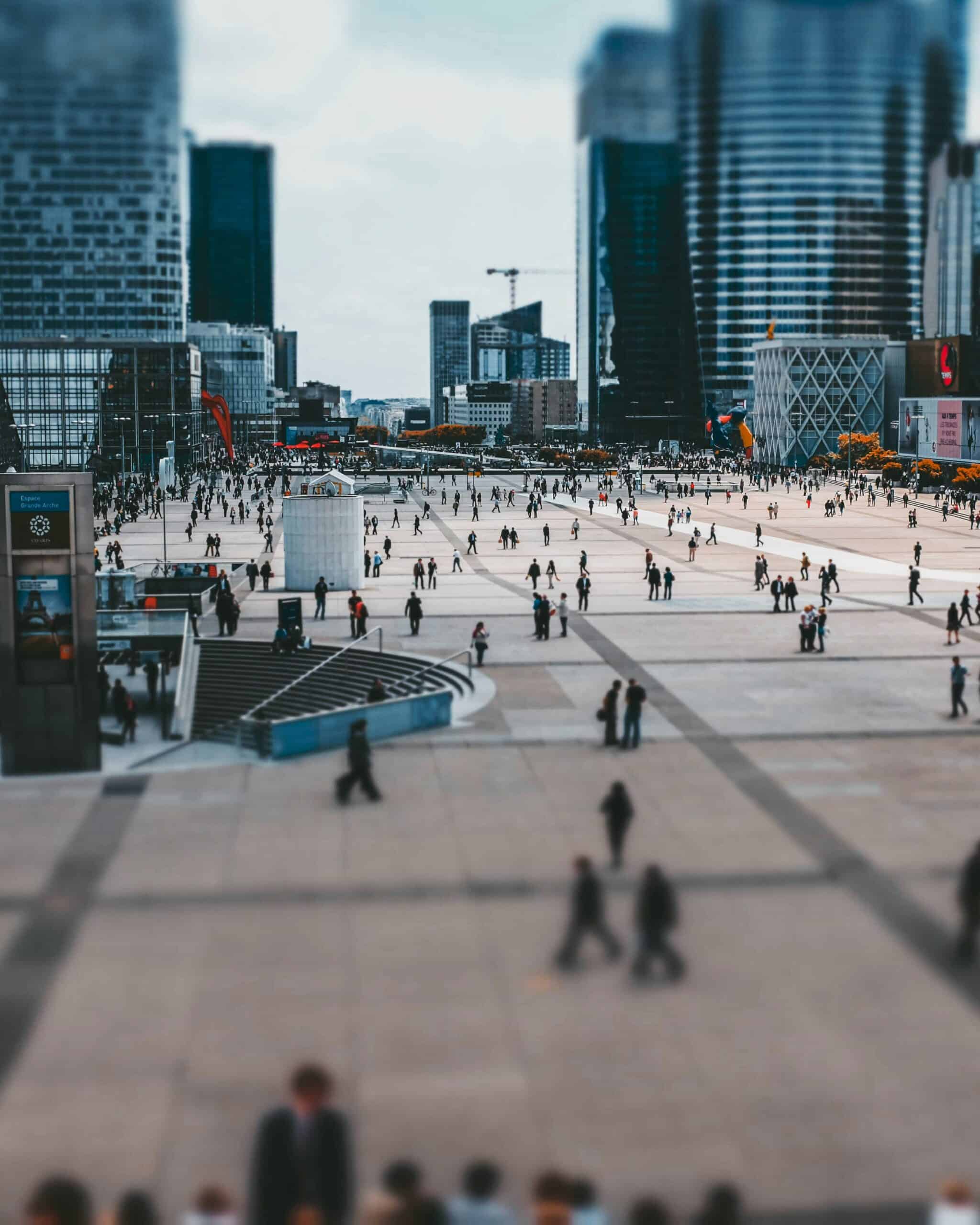 Foto em tilt shift de muitas pessoas caminhando em uma praça da cidade