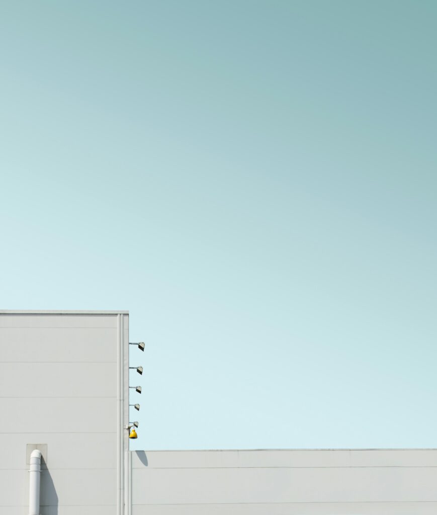 top of modern white building with yellow sconce lights against pale blue sky