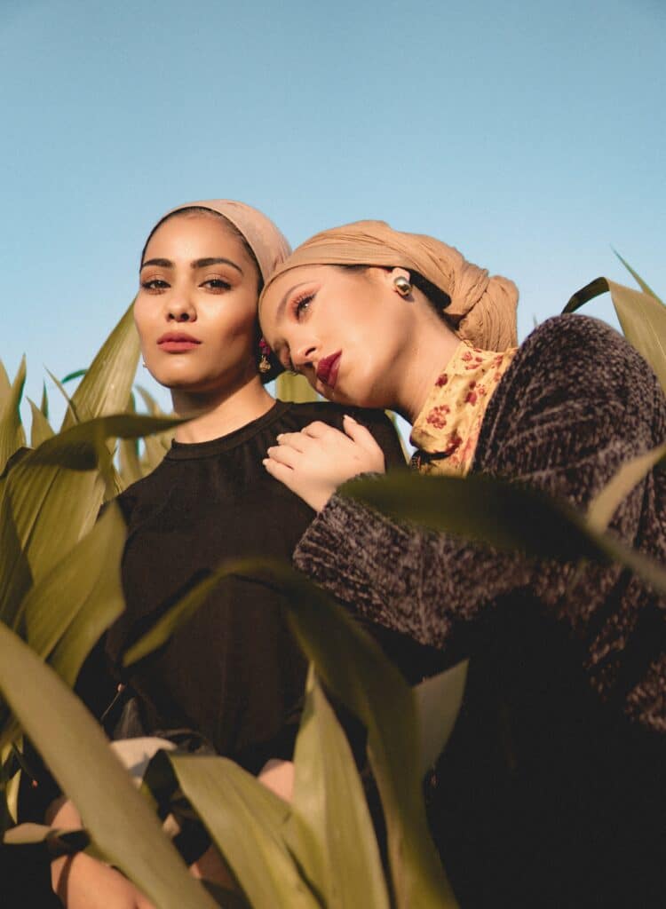 Duas mulheres posando com vestidos pretos cercadas por plantas verdes altas