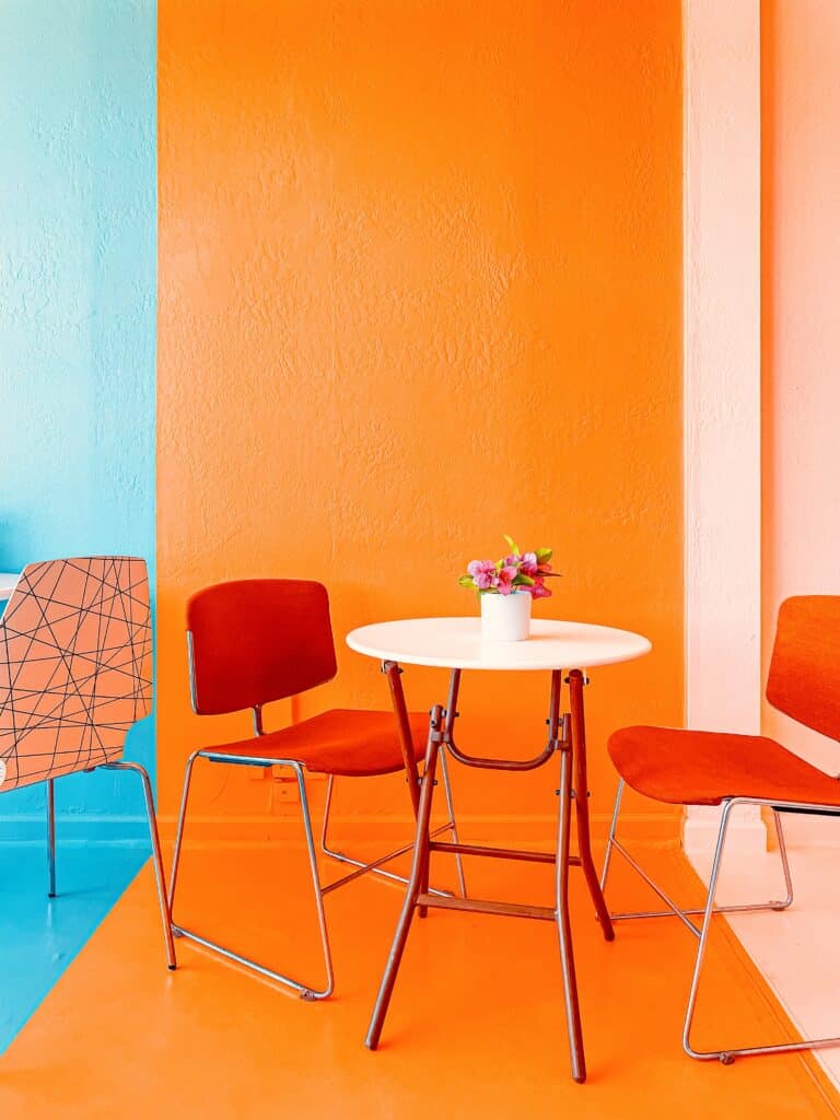 table blanche et chaises orange foncé dans une pièce peinte en orange et aqua