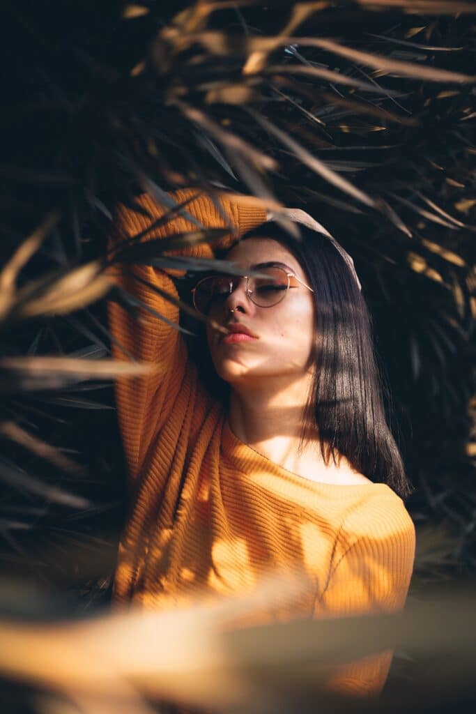 mujer con camisa amarilla y maquillaje naranja posando entre hojas con pinchos