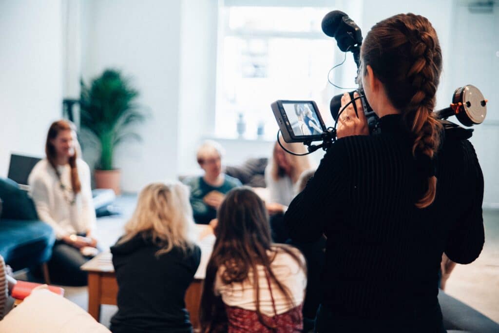 Frau dreht Video von einer Gruppe von Menschen, die um einen Tisch sitzen