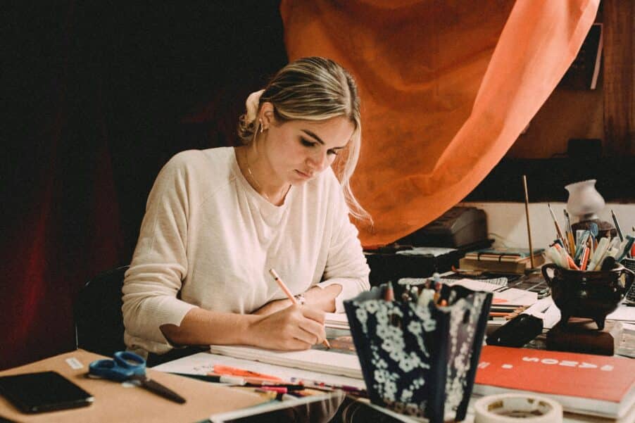 woman sitting and drawing at table in her studio scaled e1706642045346