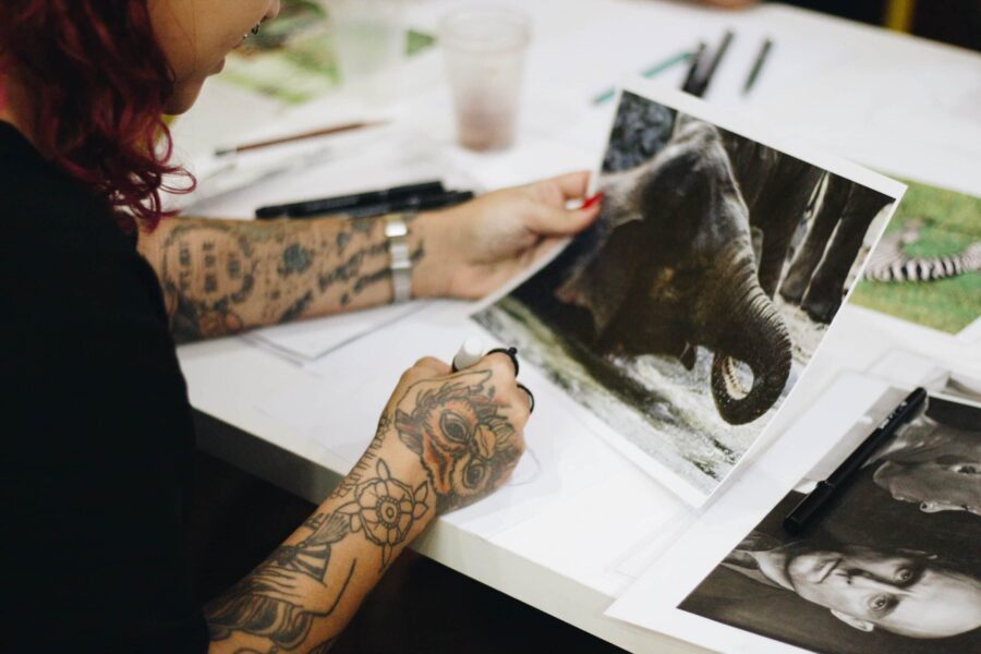 woman with tattooed arms holding a photo print of an elephant scaled e1698299272433